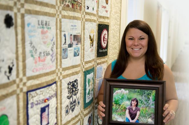 Woman holds picture of donor in front of a yellow quilt