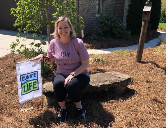 Organ recipient Julie sitting front of her house next to a Donate life Flag