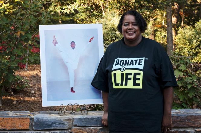 Woman with donate life t-shirt stands next to photo of donor son