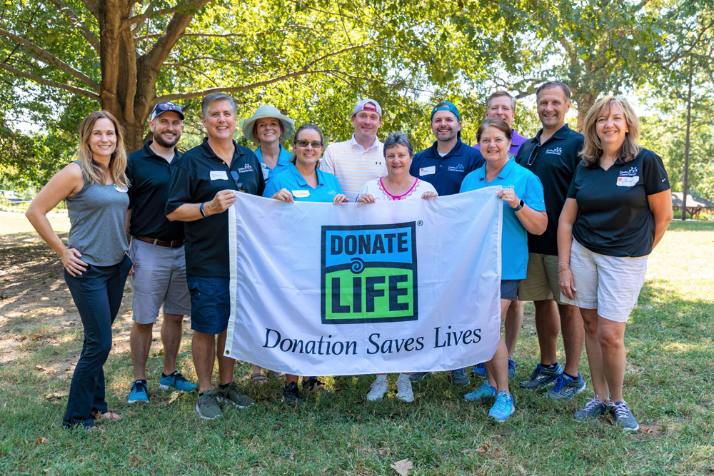 HonorBridge staff members holding a donate life flag under a shady tree