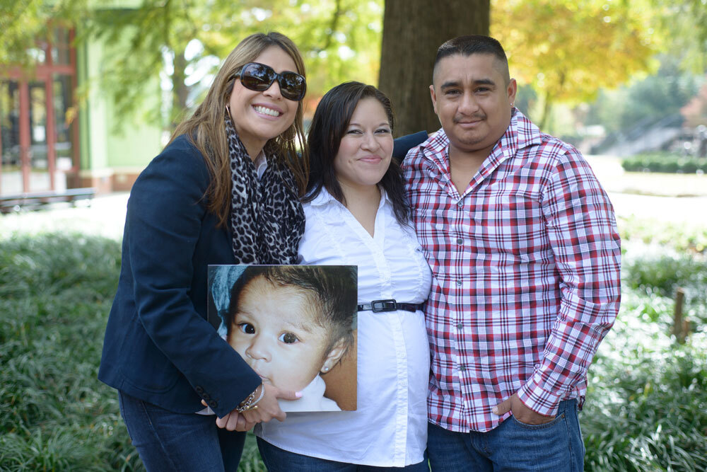 A donor family embrace and pose for a photo while holding a photo of a young child