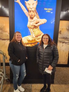 Jen and Michelle pose together in front of Lion King poster