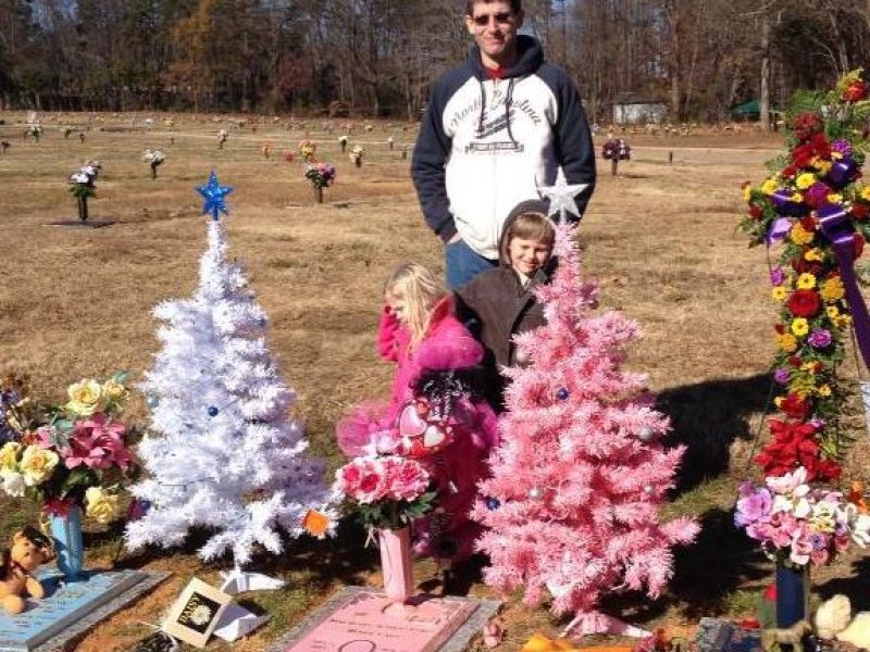 Brian Suttles standing with his two children in front of wife's grave