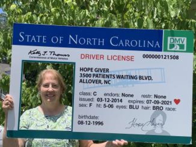 Organ recipient Beverly holding an oversized driver's license poster