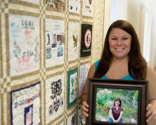 Woman holds picture of donor in front of a yellow quilt