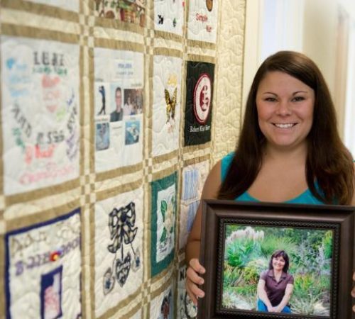 Woman holds picture of donor in front of a yellow quilt