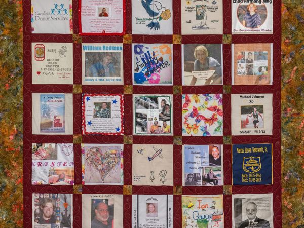 Colorful red quilt with leaf pattern and 25 unique squares featuring donor names, photos, and memories