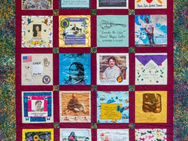 Colorful red quilt with 20 unique squares featuring donor names, photos, and memories