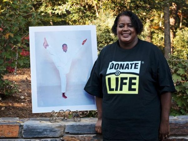 Woman with donate life t-shirt stands next to photo of donor son