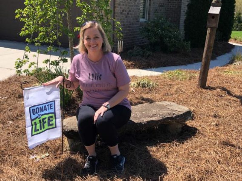 Organ recipient Julie sitting front of her house next to a Donate life Flag
