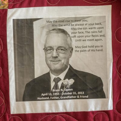 Quilt square for Bruce Ogden with portrait of Bruce in a suite and text reading: May the road rise to meet you, may the wind be always at your back, may the sun warm upon your face, the rains fall soft upon your fields and, may god hold you in the palm of his hand.