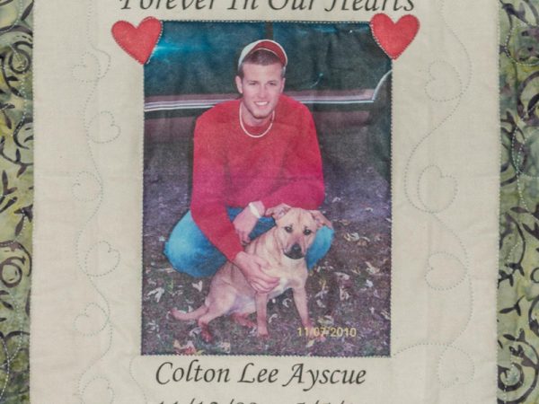 Quilt square for Colton Ayscue with a photo of Colton and his dog and two hearts in the corner.