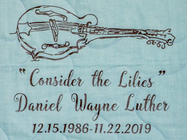 Quilt square for Daniel Luther with guitar and text reading: Consider the Lilies.
