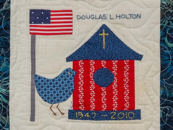 Quilt square for Douglas L Holton with an American flag, a bird feeder with a cross, and a bird.