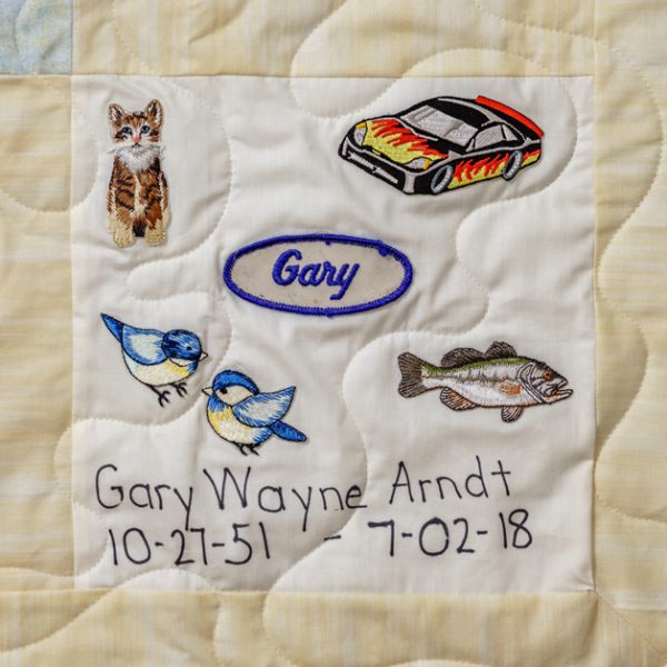 Quilt square for Gary Wayne Arndt with patches of a cat, nascar, birds, and a fish