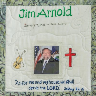 Quilt square for Jim Arnold with a photo of Jim and patches of a violin and a cross. Text reading: As for me and my house we shall serve the Lord. Joshua 24:15