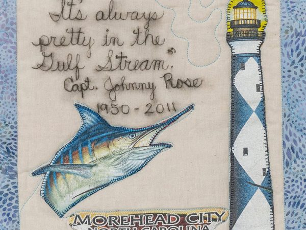Quilt square for John Rose with patches of a sword fish, a lighthouse, Morehead city North Carolina, and text reading: It’s always pretty in the gulf stream. Capt. Johnny Rose.