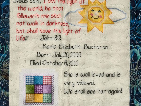 Quilt square for Karla Buchanan with sun and cloud, quote from John 8:2, and text reading: She is well loved and is very missed. We shall see her again!