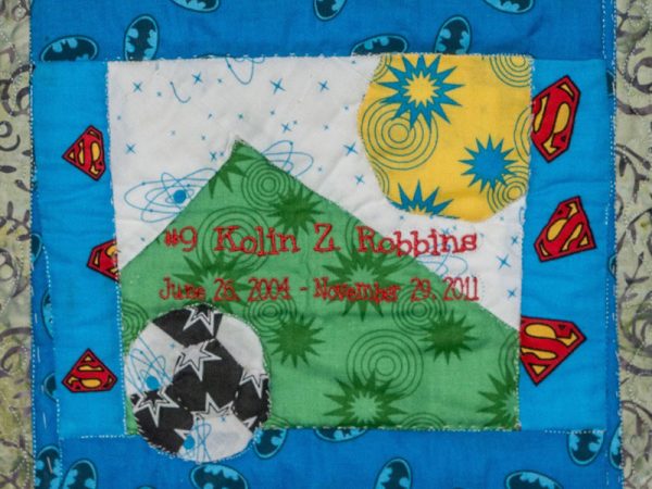 Quilt square for Kolin Robbins with colorful superhero logos, a soccer ball, a mountain and a sun.