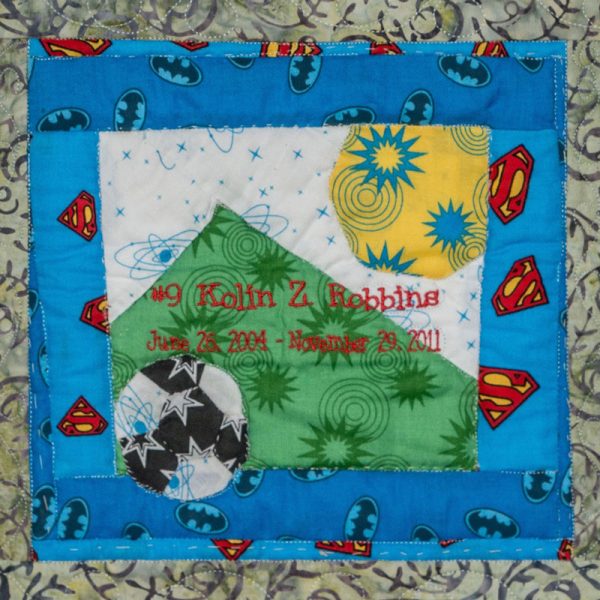 Quilt square for Kolin Robbins with colorful superhero logos, a soccer ball, a mountain and a sun.