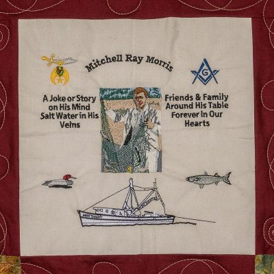 Quilt square for Mitchell Morris with small patches and text reading: A joke or story on his mind, salt water in his veins. Friends & family around his table forever in our hearts. And a patch of Mitchell holding a fishing net.