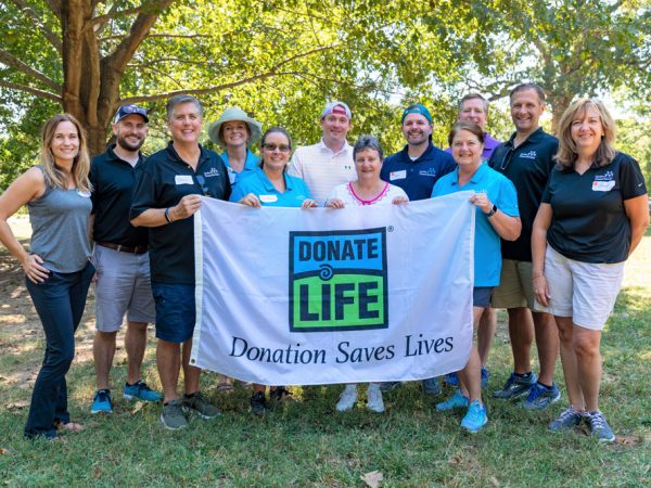 HonorBridge staff members holding a donate life flag under a shady tree