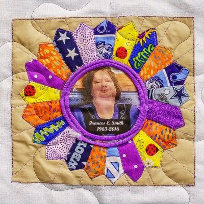 Quilt square for Frances Smith with a portait of Frances at the center of several different patches including from materials for UNC, Dallas Cowboys, lady bugs, and other various patterns.