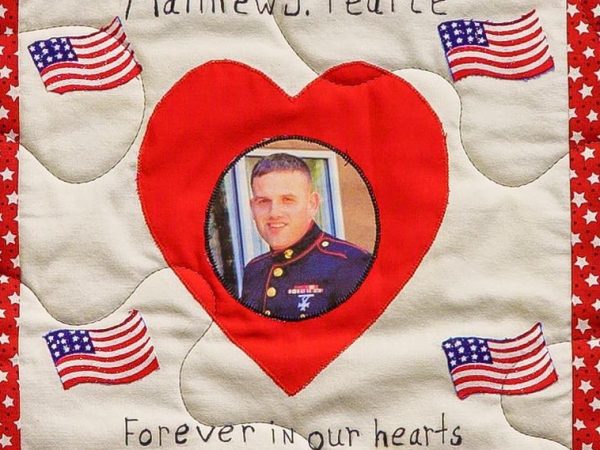 Quilt square for Matthew J. Pearce with a portrait of Matthew in his Marine Corps uniform centered in a heart and surrounded by patches of the American flag.