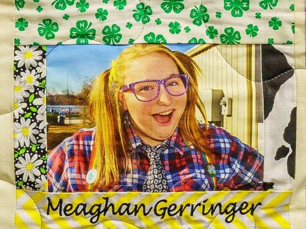 Quilt square for Meaghan Gerringer with patterns of four leaf clover, flowers, and a portrait of Meaghan.